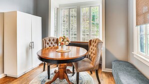 A dining area with a round table, two upholstered chairs, a bench, and a white cabinet.