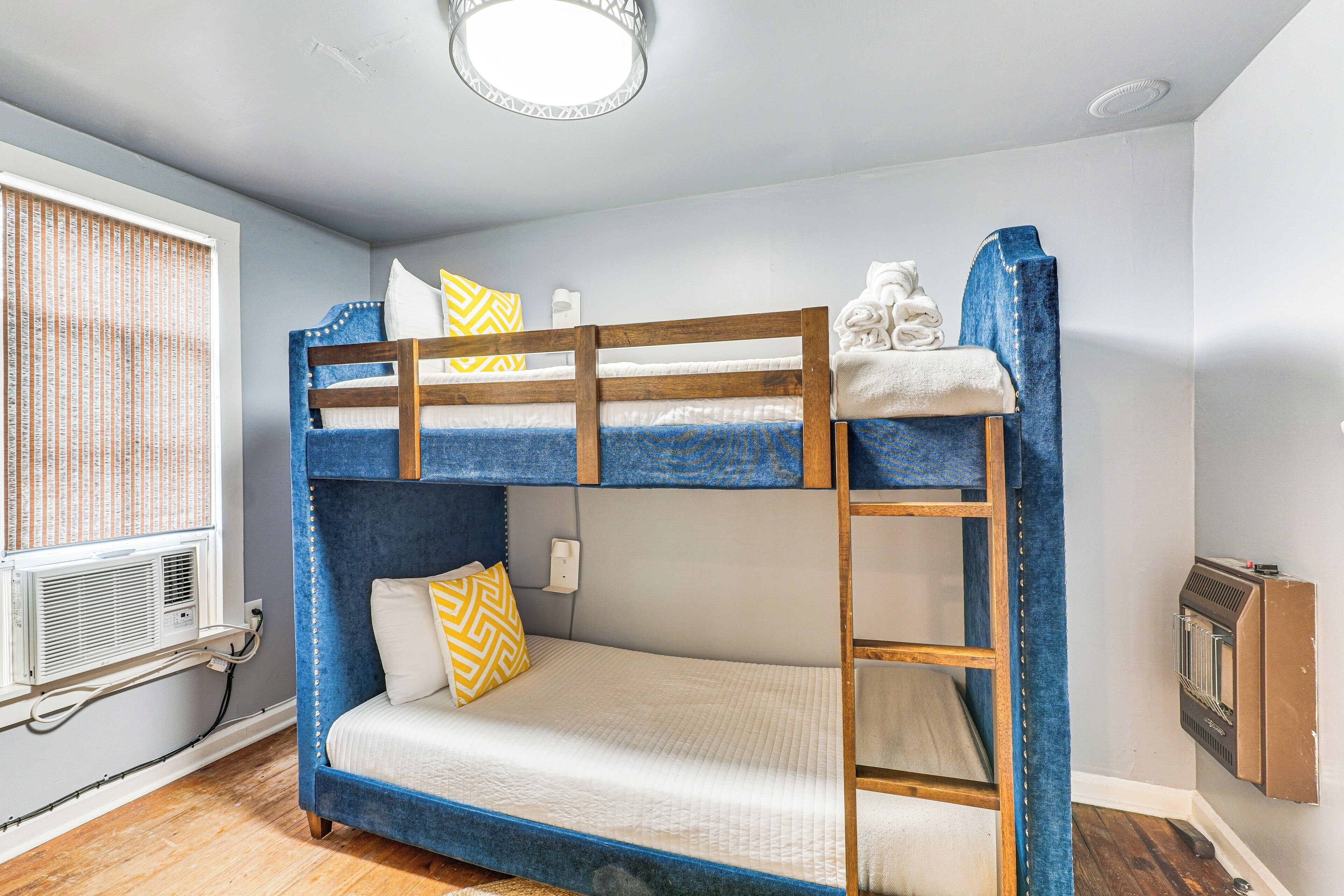 Dormitorio con literas, ventana, aire acondicionado y radiador.