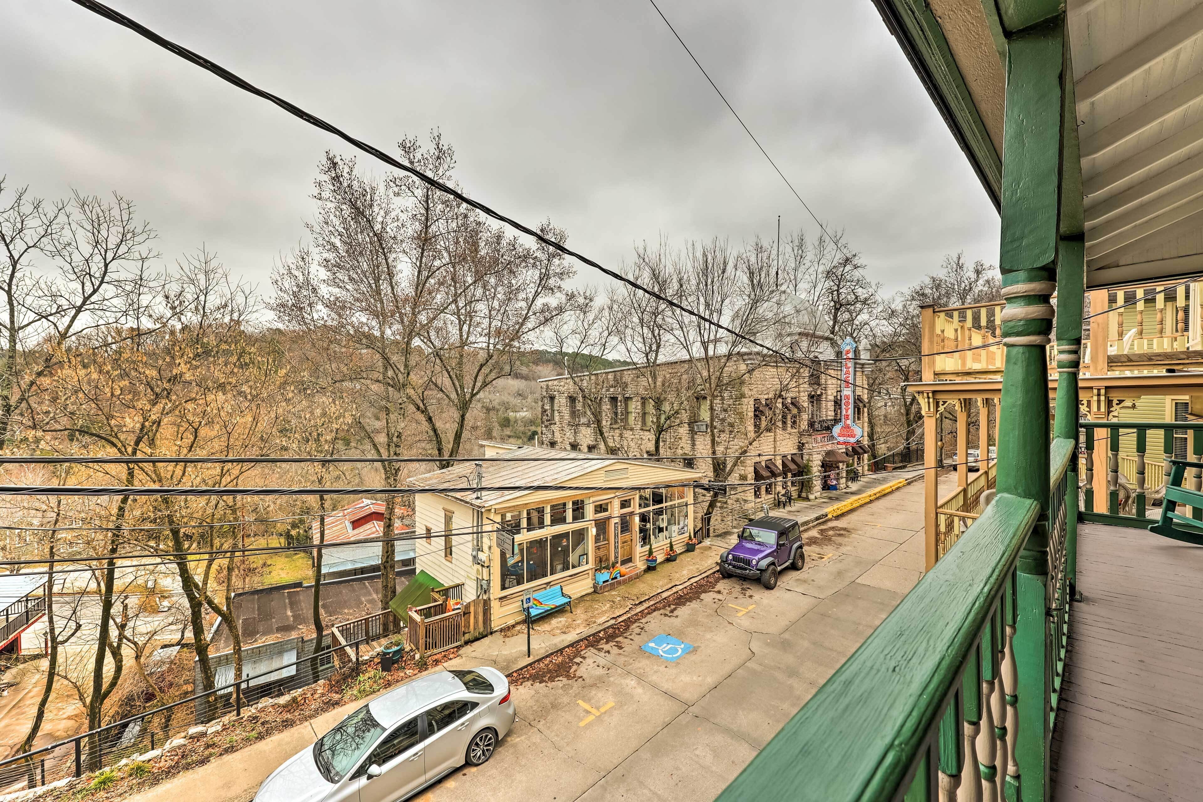 Vista desde un balcón sobre una calle con un edificio que tiene un porche y un coche estacionado.