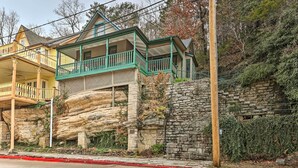 A two-story house with a balcony, stone foundation, and a red curb.