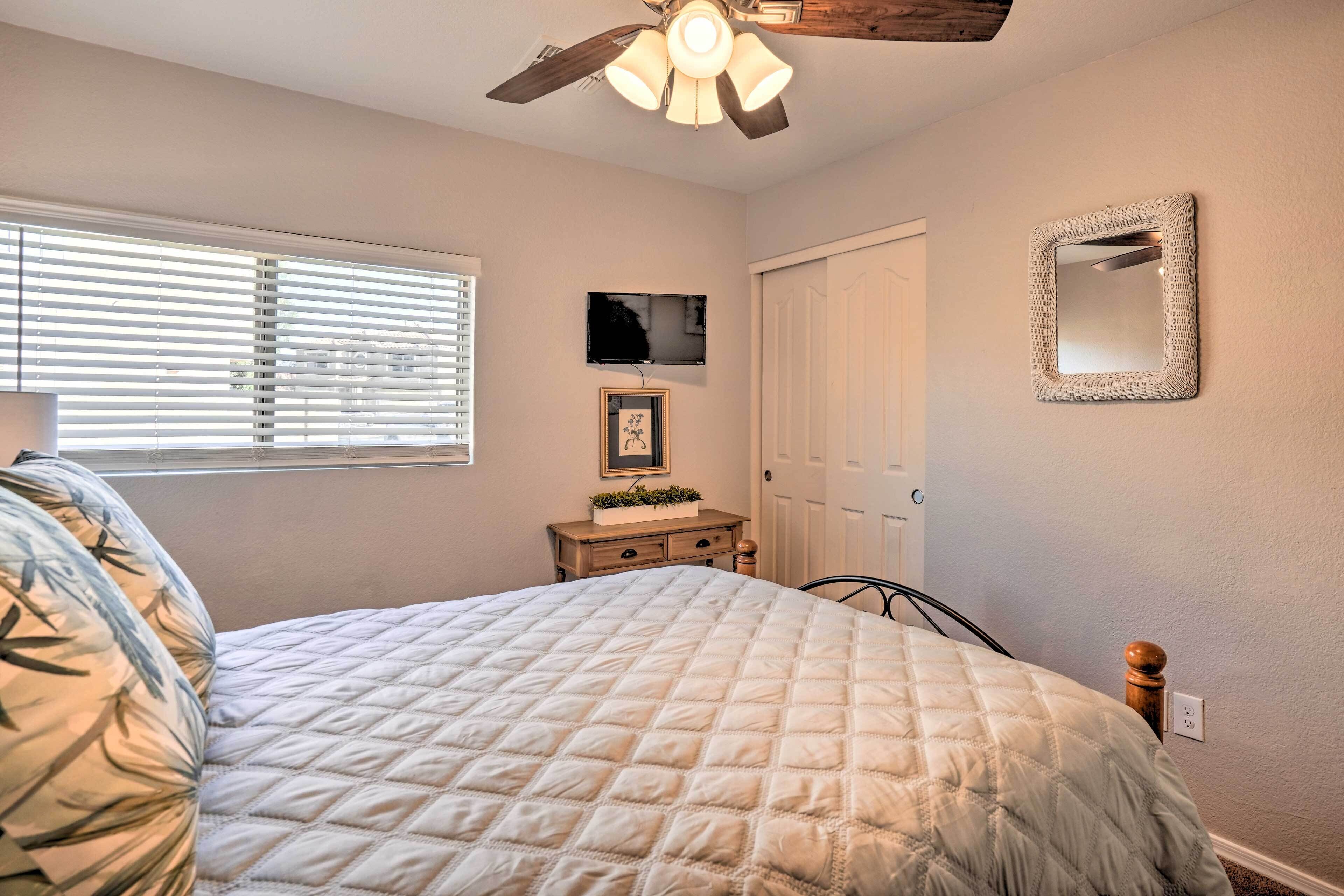 A bedroom with a bed, a ceiling fan, a TV, a dresser, and a mirror.