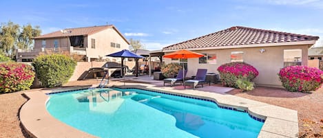 A swimming pool with a curved edge, surrounded by a patio area with lounge chairs and umbrellas.