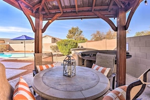 A covered patio area with a round table and chairs, a barbecue grill, and a pool in the background. - 2 Mi to State Farm Stadium: Phoenix Retreat (Phoenix)