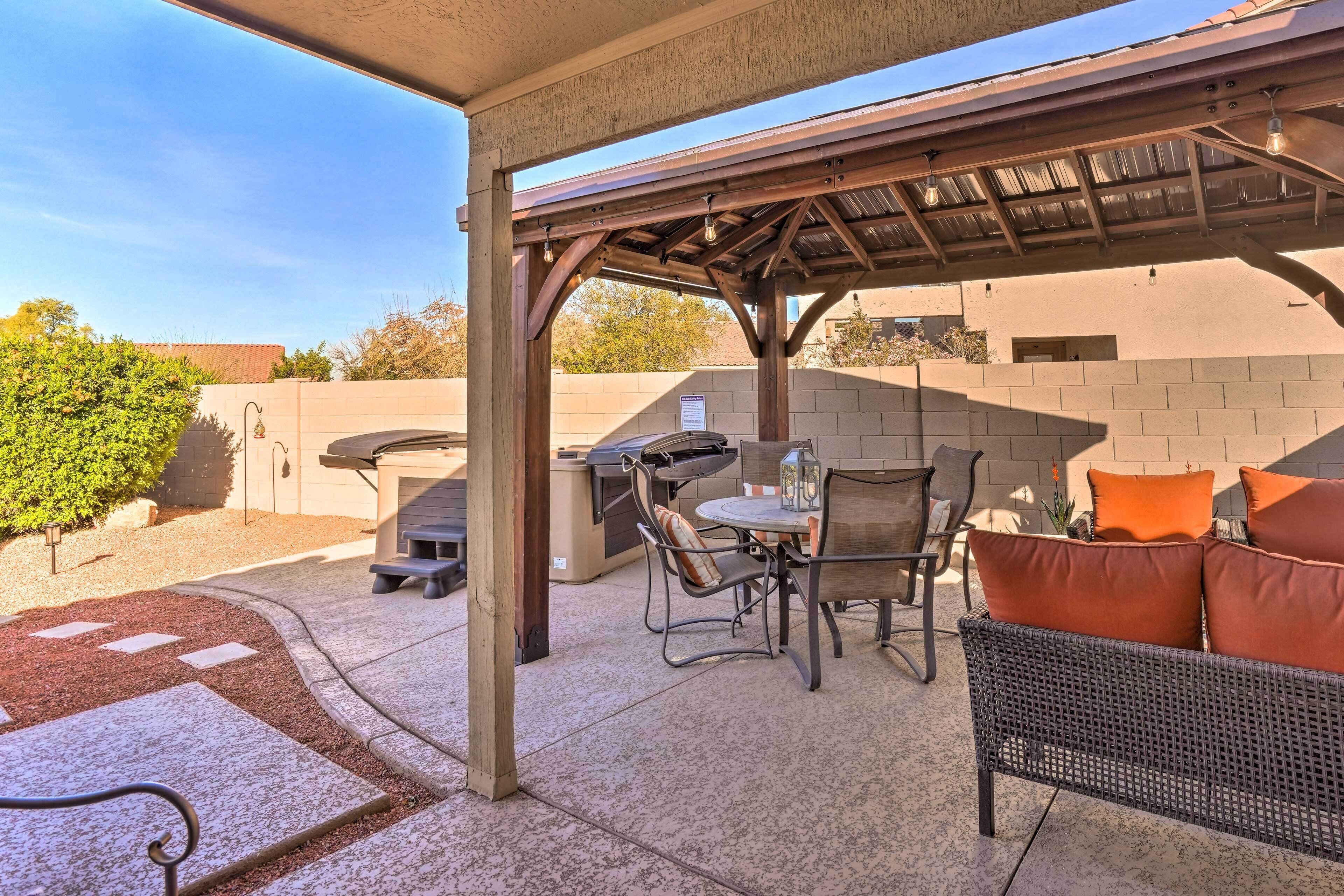 Een terras buiten met een barbecue, zitplaatsen en een pergola.