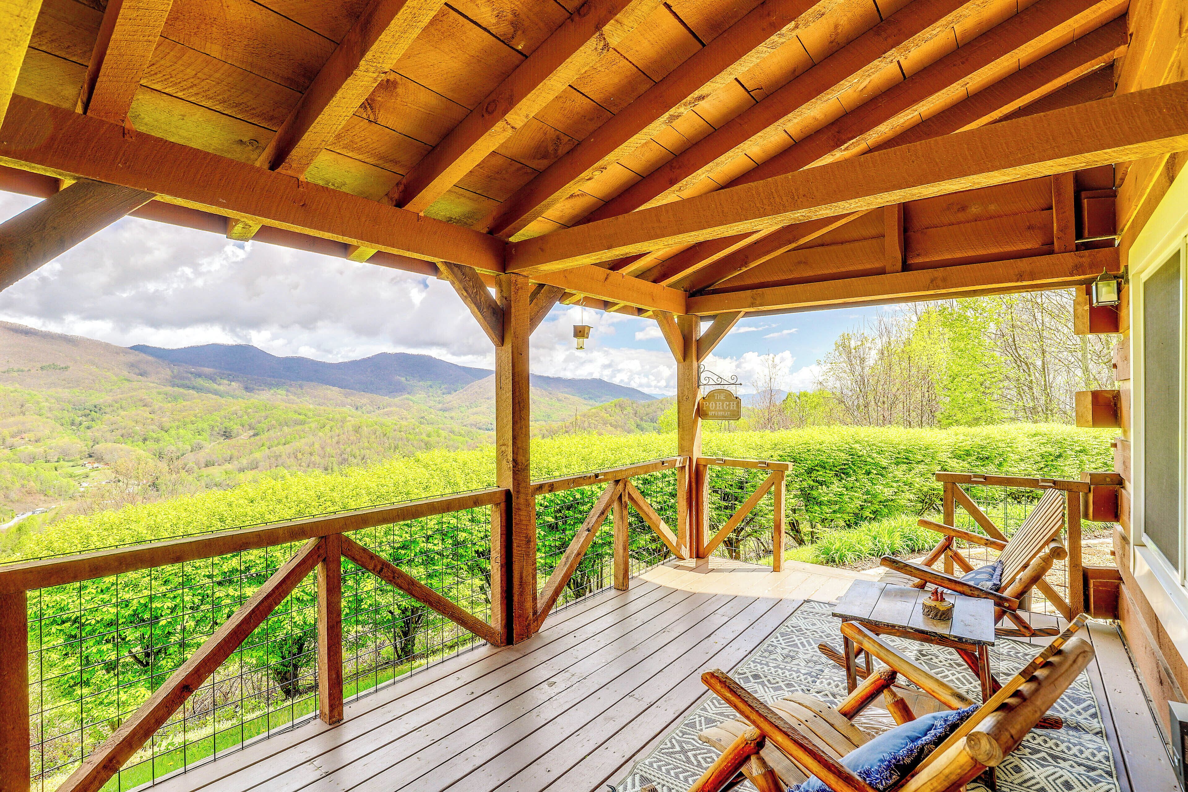 Eine Holzterrasse mit Tisch und Stühlen, die auf eine grüne Landschaft mit Bergen im Hintergrund blickt.