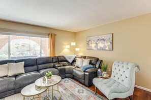 A living room with a sectional sofa, a round coffee table, and a tufted armchair. - Private Pool & Fire Pit! Walkable Tucson Retreat (Tucson)