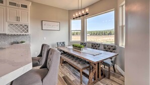 A dining area with a wooden table and grey upholstered chairs, a chandelier, and a view of a vineyard through large windows. - Vistas Bonitas Home w/ Patio: 7 Mi to Snowbowl! (Flagstaff)