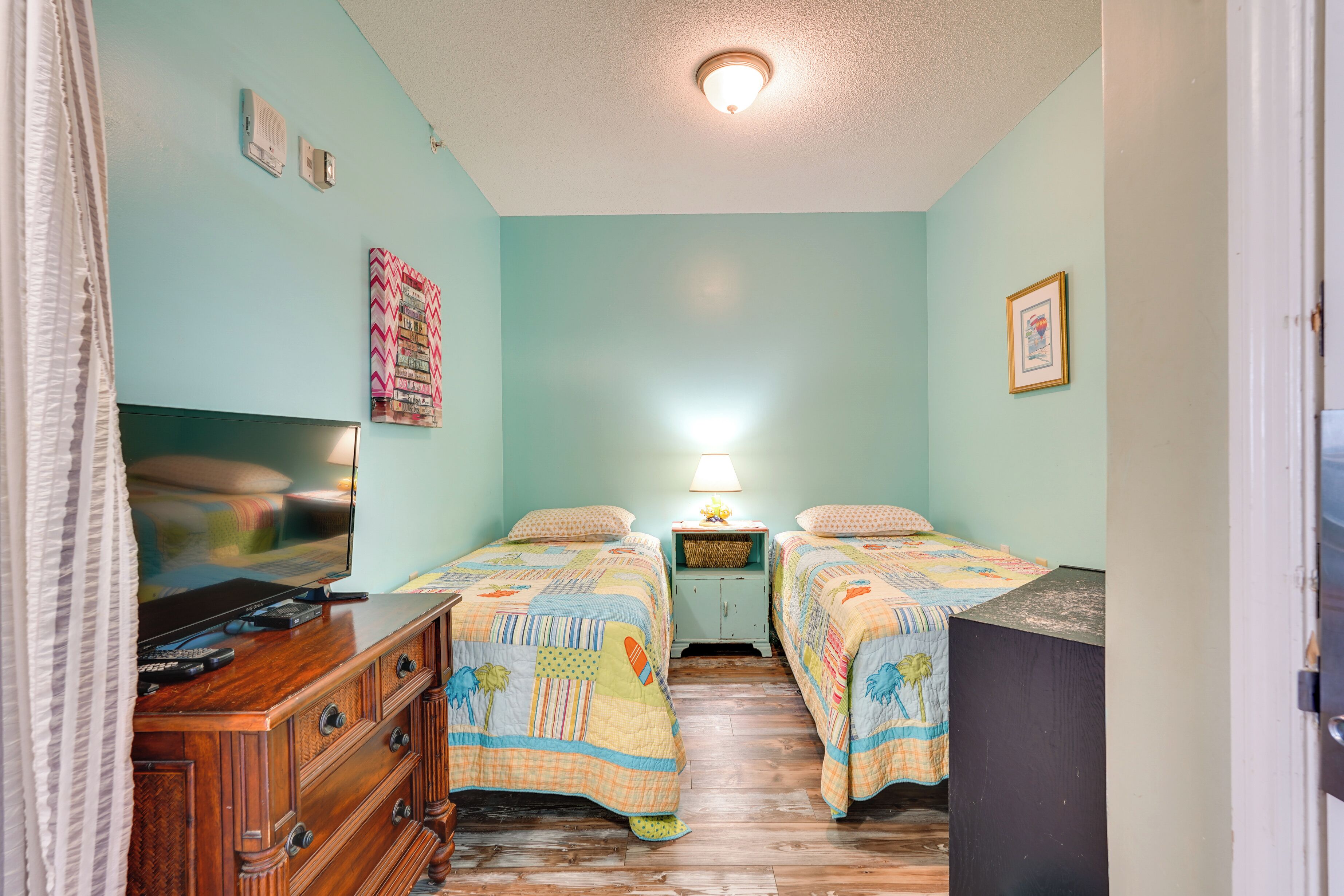 A room with two beds, a dresser, a TV, and a lamp.