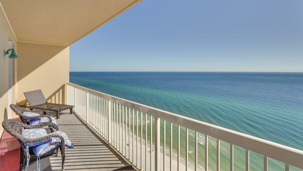 A balcony with wicker chairs and a table, overlooking a beach and the ocean. - Gulf Coast Getaway w/ Balcony & Resort Amenities! (Panama City Beach)