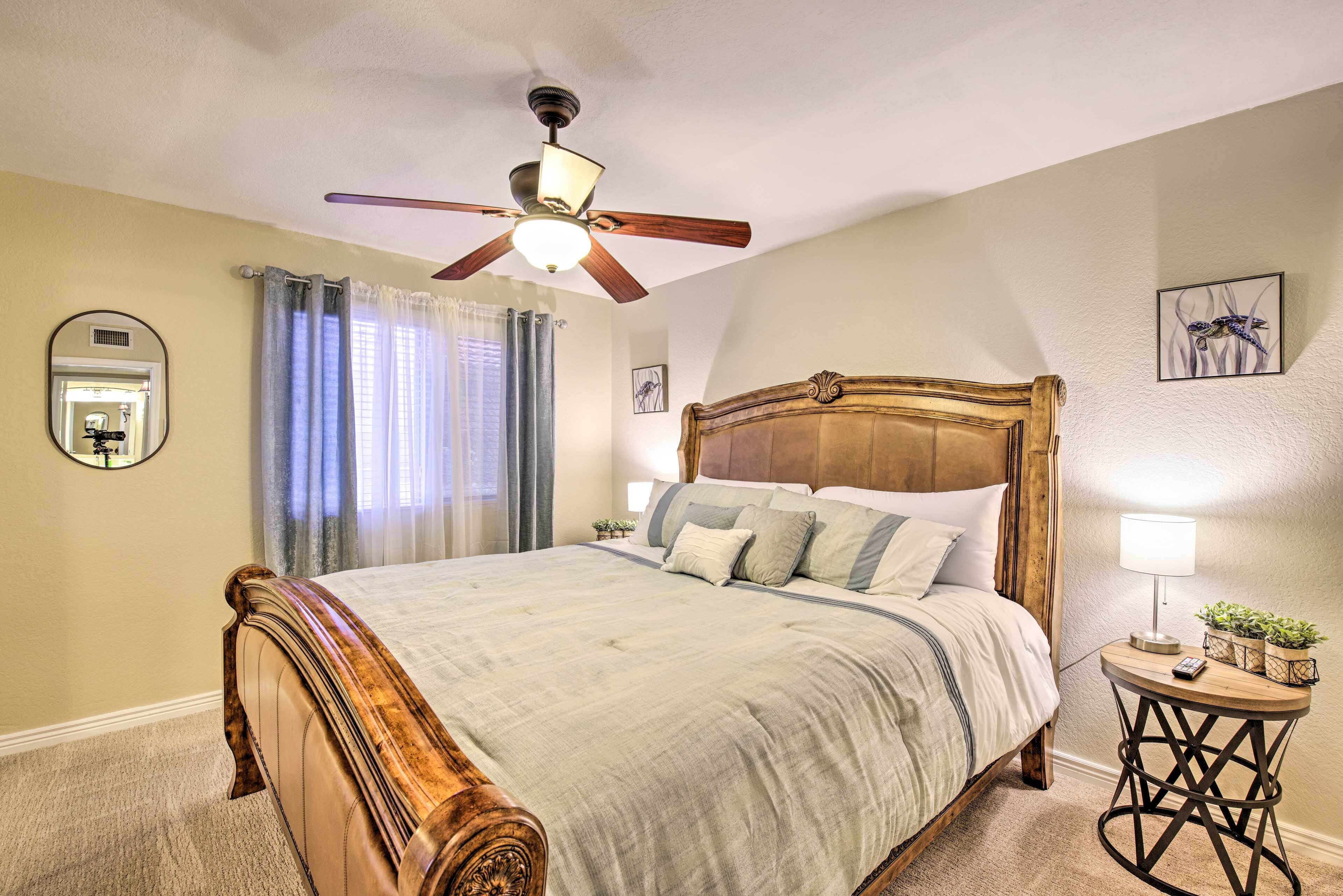 A bedroom with a large bed, a ceiling fan, a bedside table with a lamp, and a small plant.