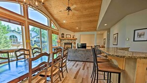 A spacious dining area with a long wooden table and chairs, a stone fireplace, and a large window overlooking a scenic view. - Mountain Home With Decks, Walk to Gondola (Steamboat Springs)