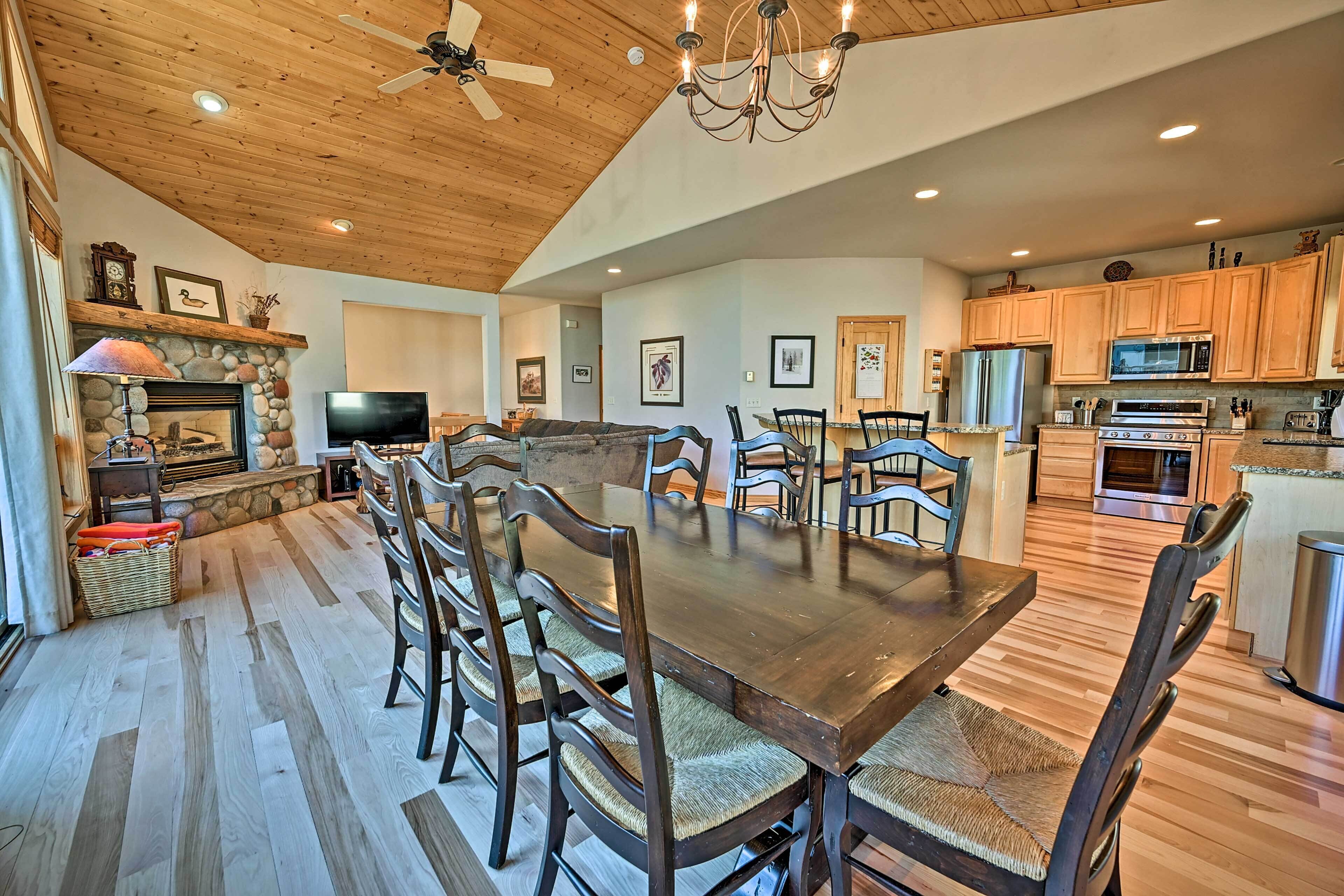 A spacious kitchen with wooden cabinets, a dining area with a large table and chairs, a stone fireplace, and a ceiling fan.
