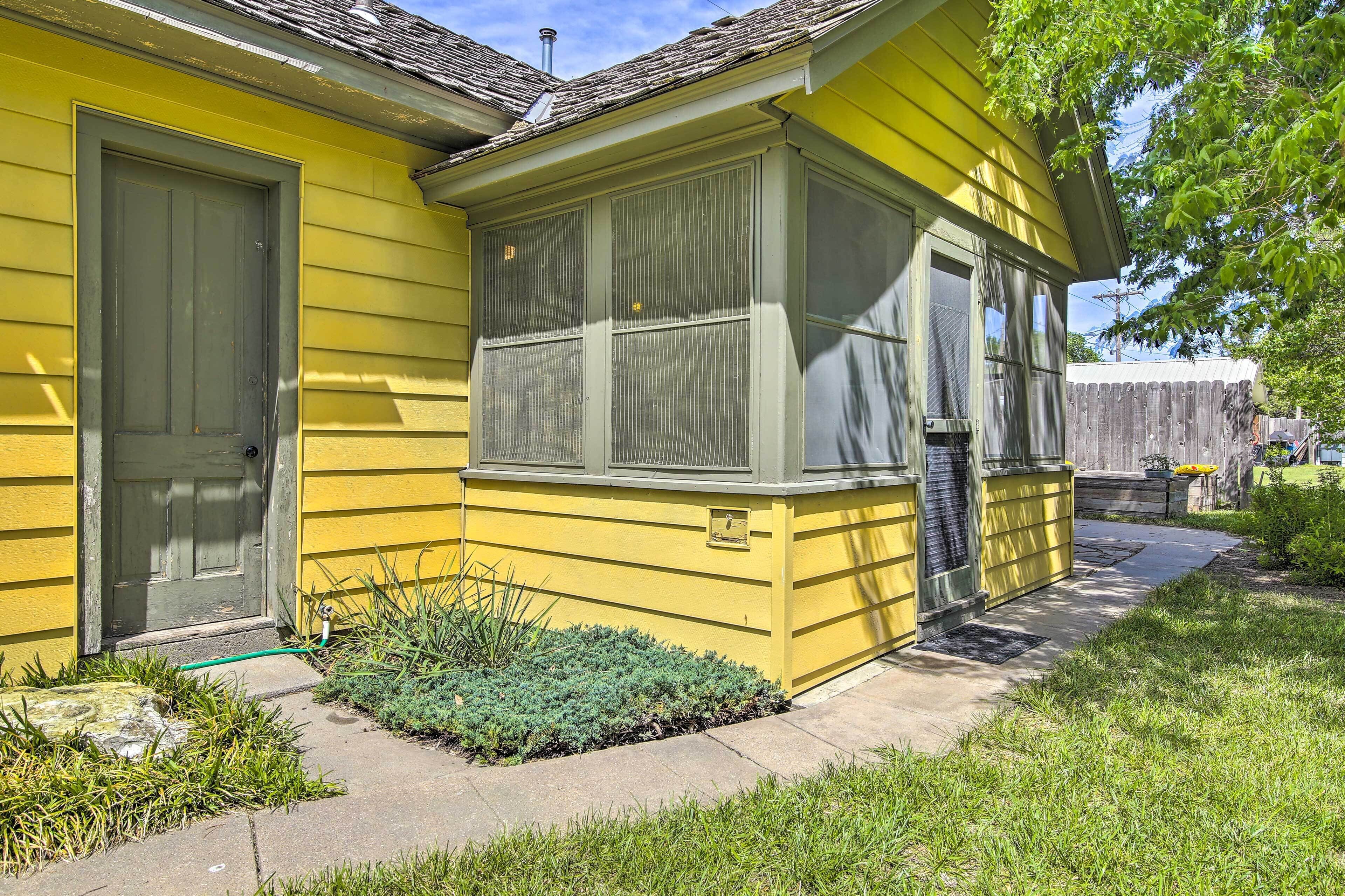 A yellow house with a front door, a covered porch, and a small garden area.