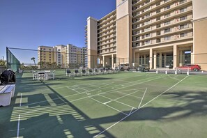 A tennis court with a net, surrounded by a fence, and adjacent to a multi-story hotel building. - Beachfront Resort Condo w/ Panoramic Ocean Views! (New Smyrna Beach)