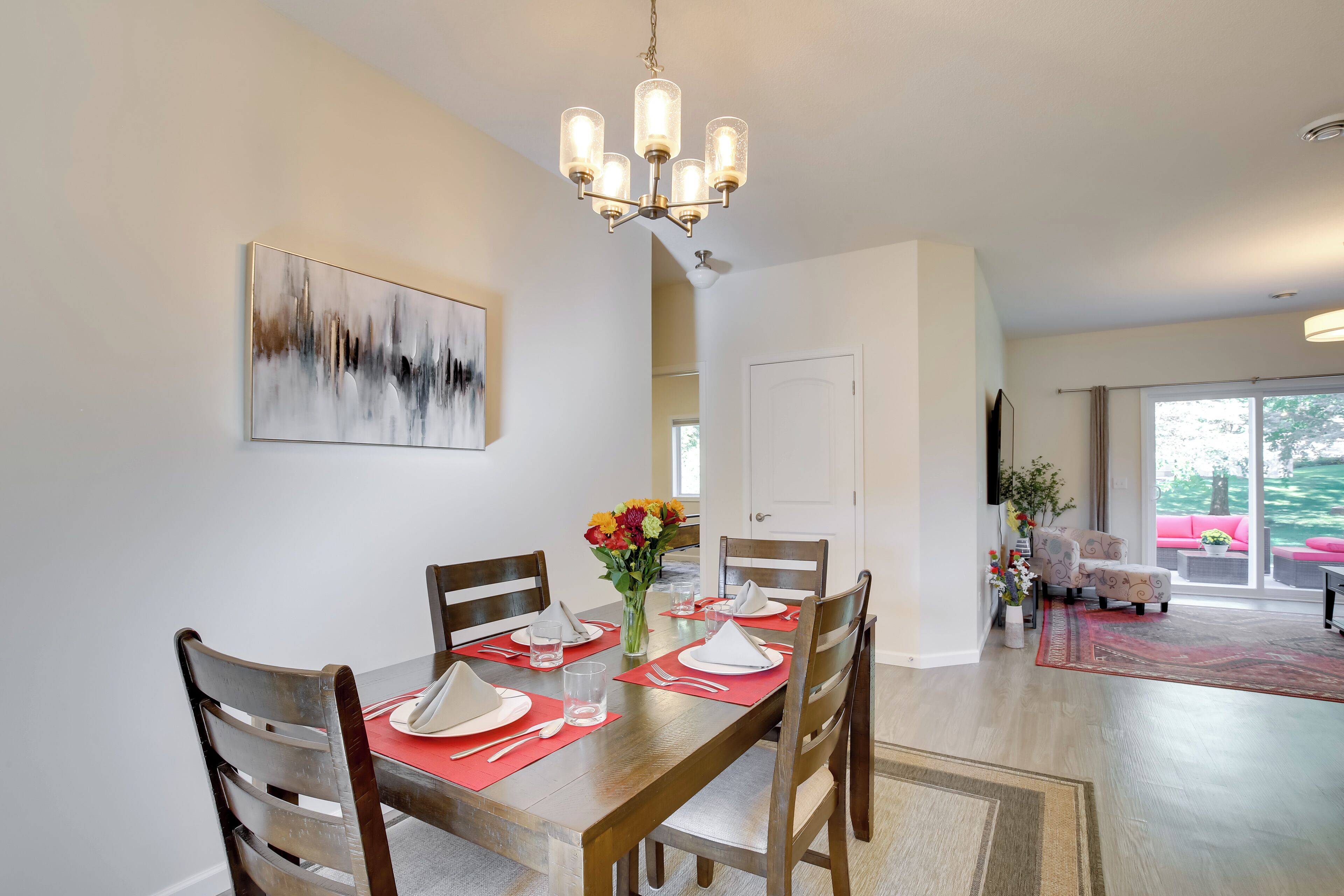 A dining area with a wooden table set for four, a chandelier, and a painting on the wall.