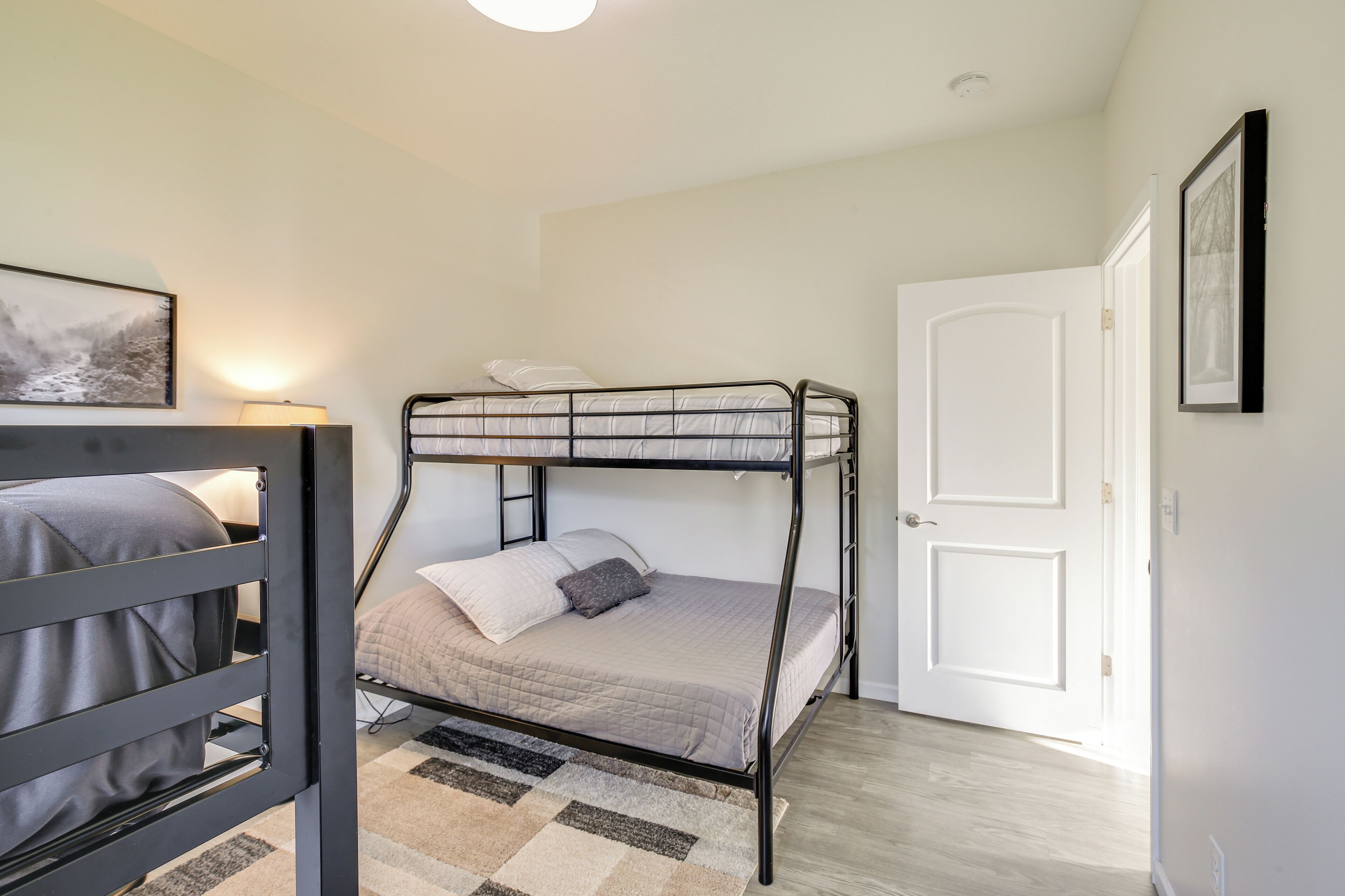 Habitación con literas, un tapete de cuadros, un cuadro en la pared y una puerta blanca.