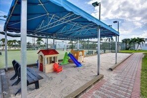 A covered play area with a slide, benches, and a small building.