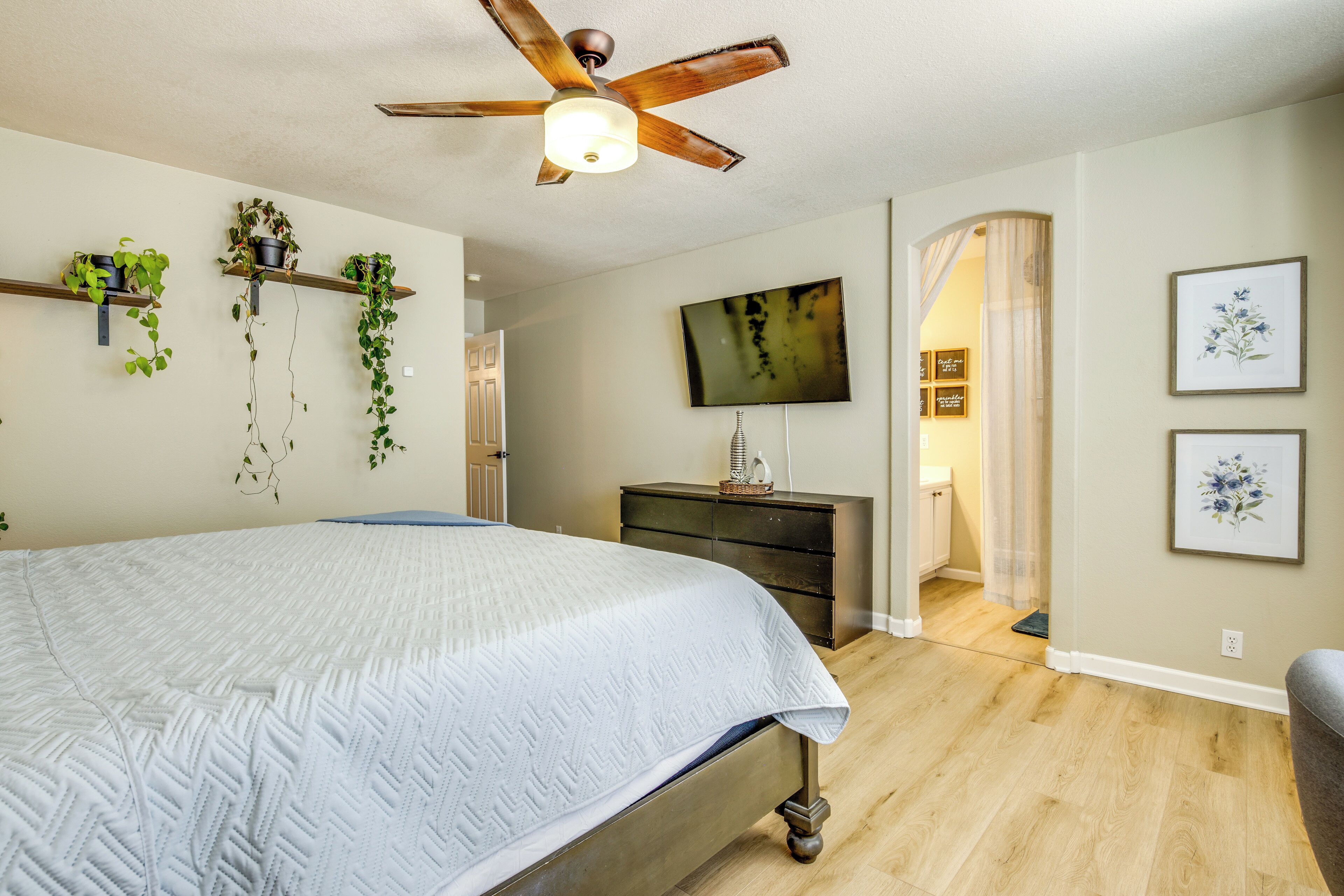 Une chambre à coucher avec un lit, un ventilateur de plafond, une télévision et des étagères murales ornées de plantes.