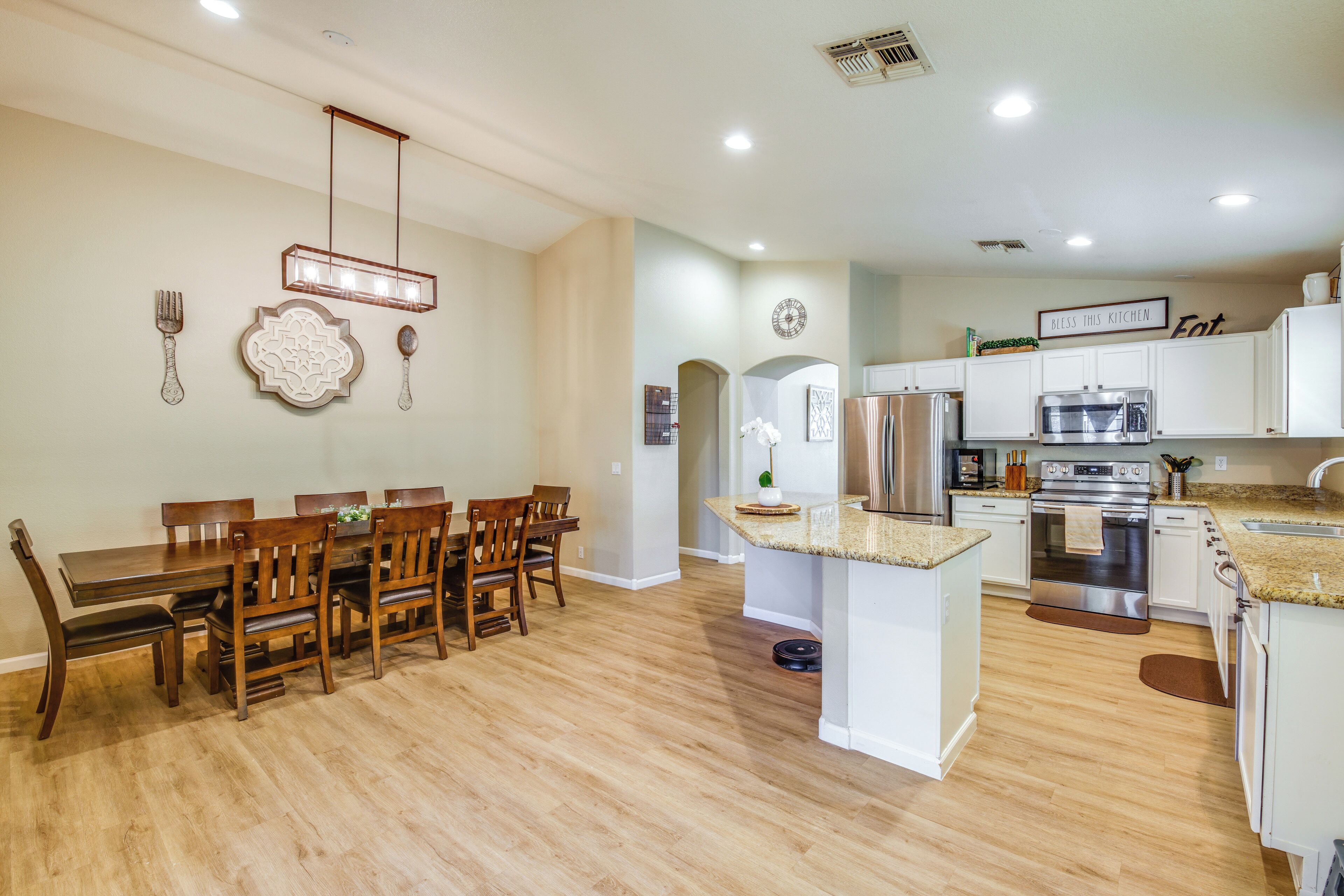Una cocina moderna con armarios blancos, electrodomésticos de acero inoxidable y un comedor con sillas y mesa de madera.
