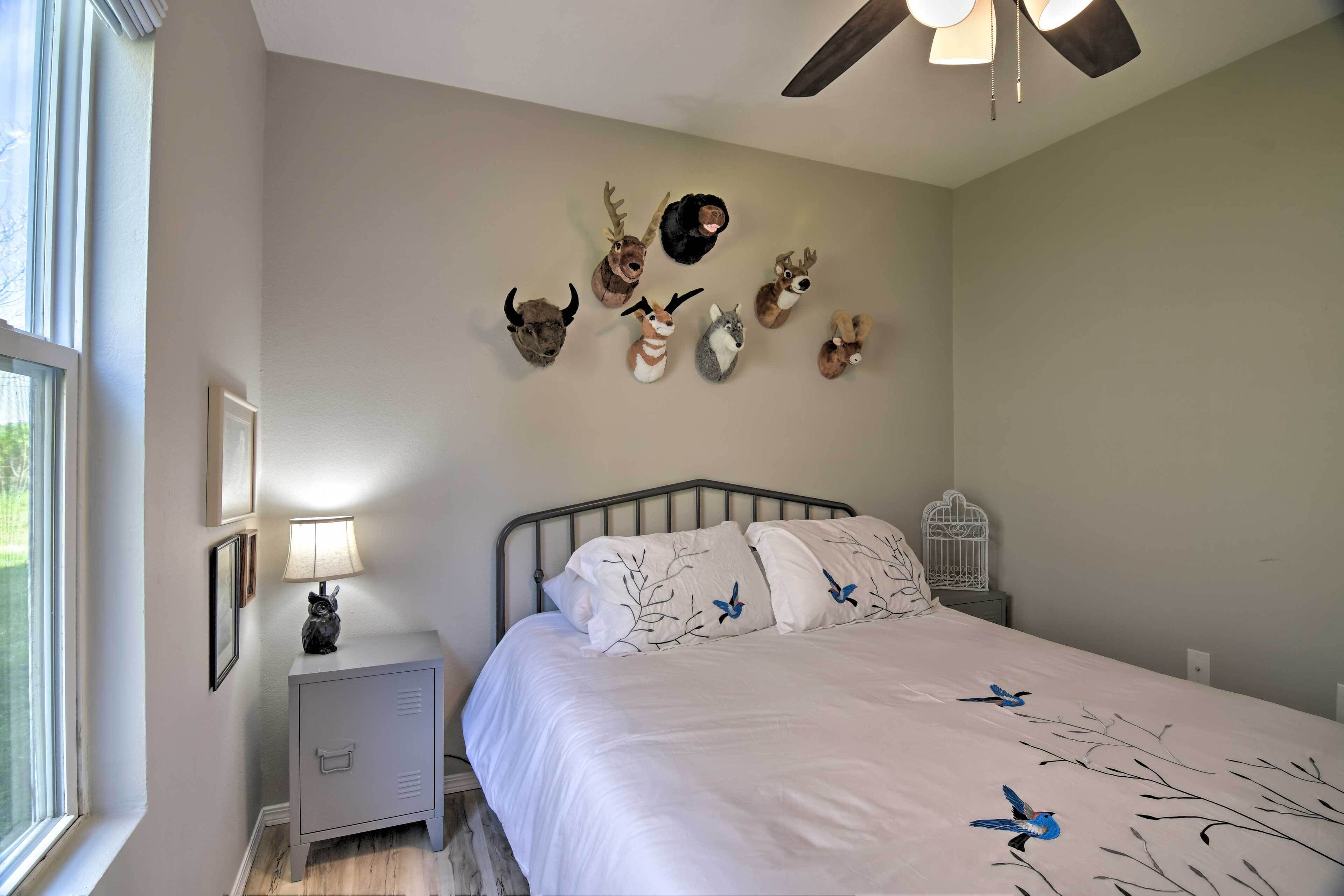 A bedroom with a bed, a nightstand, a lamp, a ceiling fan, and wall-mounted animal head decorations.