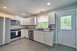 A modern kitchen with white cabinets, stainless steel appliances, a granite countertop, and a window with blinds.