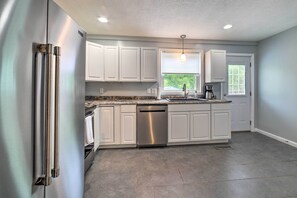 A modern kitchen with white cabinets, stainless steel appliances, a dishwasher, and a window providing natural light.