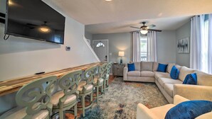 Ein Wohnzimmer mit Ecksofa, einem flachbildfernseher an der Wand, einem Deckenventilator und einem Essbereich mit Holztisch und Stühlen.