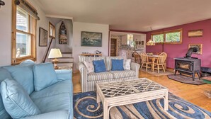 Una sala de estar acogedora con un sofá azul, un sofá a rayas y una mesa de centro de madera. Hay un comedor con una mesa y sillas, y una cocina con estufa.
