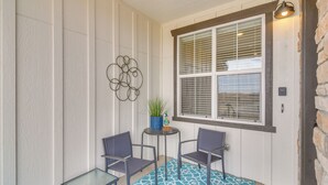 Une petite terrasse avec deux chaises et une table, un pot de fleurs et une fenêtre avec des stores.