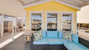 A covered outdoor seating area with a wicker sofa and a small table, large windows, and a view of the surrounding area. - Steps to Beach: Lake Havasu City Home w/ Grill! (Lake Havasu City)