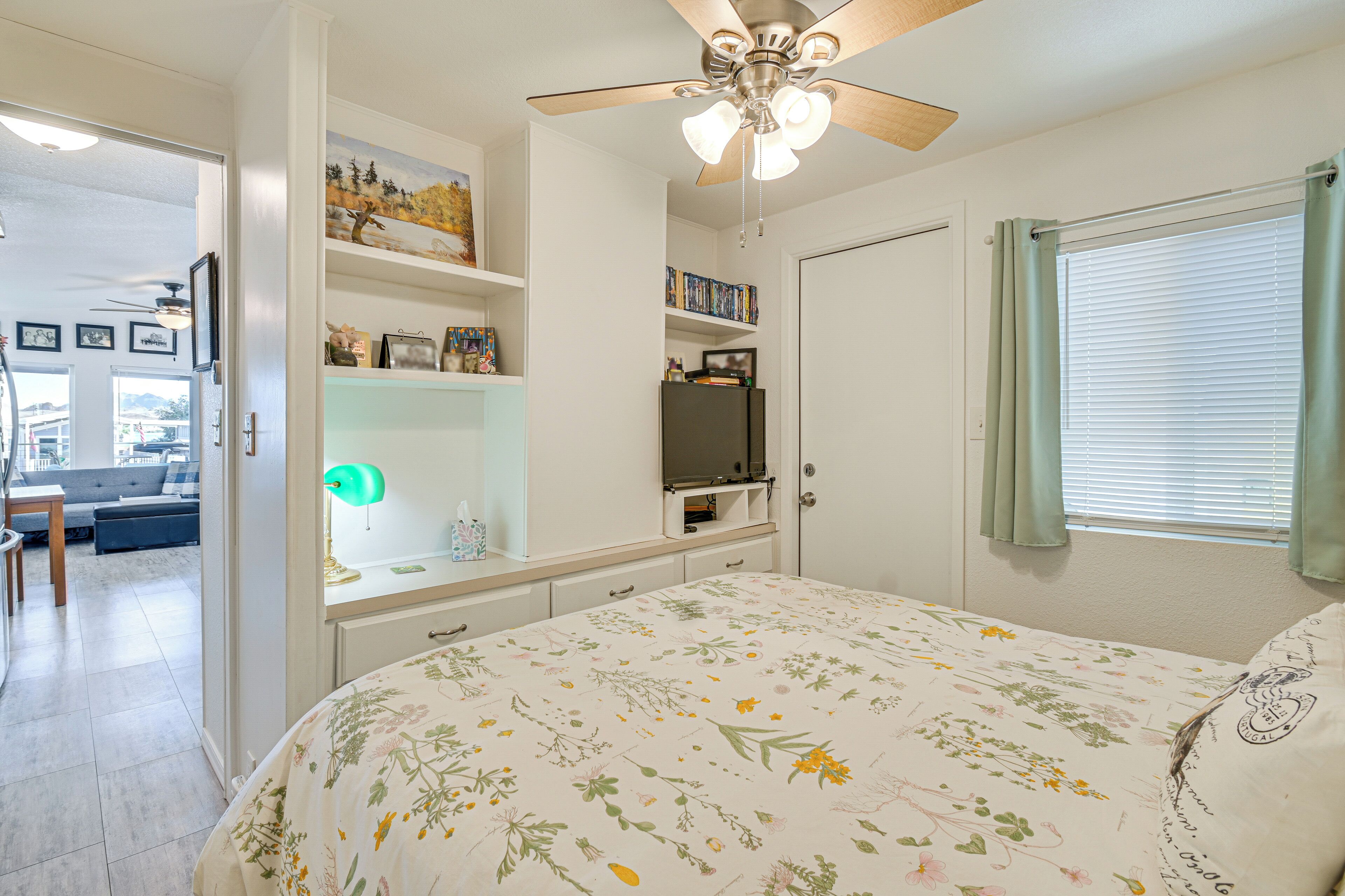 A bedroom with a bed, a ceiling fan, a TV, and a window with curtains.
