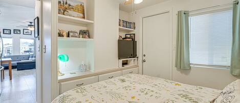A bedroom with a bed, a ceiling fan, a TV, and a window with curtains.