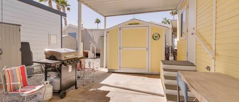 A covered patio area with a grill, a chair, and a table.