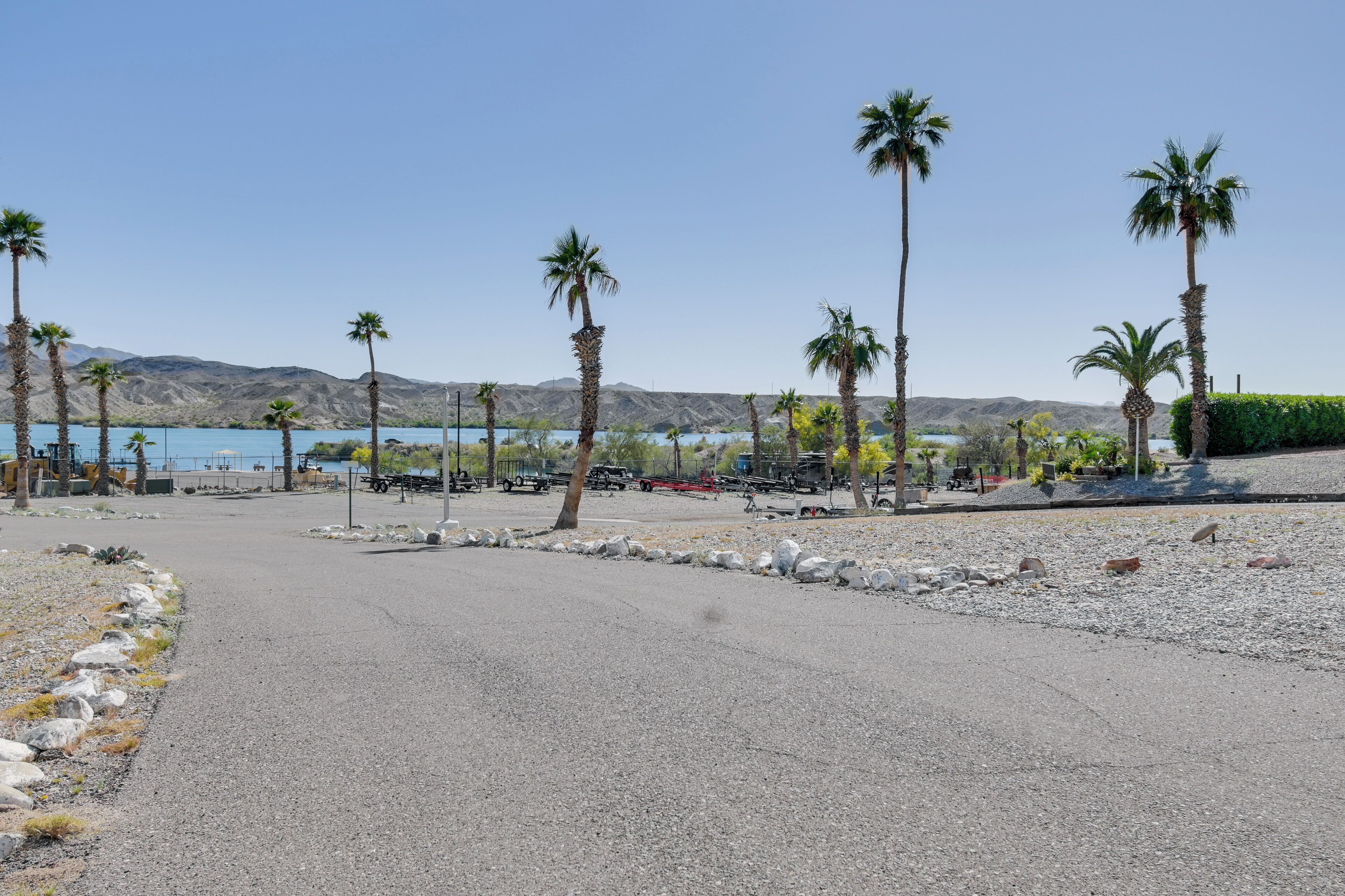 A paved parking area with palm trees and a view of a lake and mountains in the background.