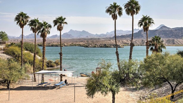 A beach with palm trees, a tent, and a boat by the water. - Steps to Beach: Lake Havasu City Home w/ Grill! (Lake Havasu City)