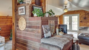 Ein gemütliches Blockhauss-Interieur mit Holzwand, Deckenventilator, Fernseher und einer komfortablen Sitzgruppe.