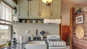 Eine Küche mit Gasherd, Backofen und Arbeitsplatte aus Granit. Über der Spüle befinden sich Schränke und ein Fenster mit Jalousien.