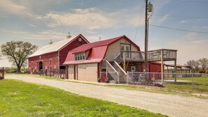 Ein rotes Bauernhaus mit großer offener Tür, einer Veranda und einem eingezäunten Bereich mit einem roten Wagenrad.