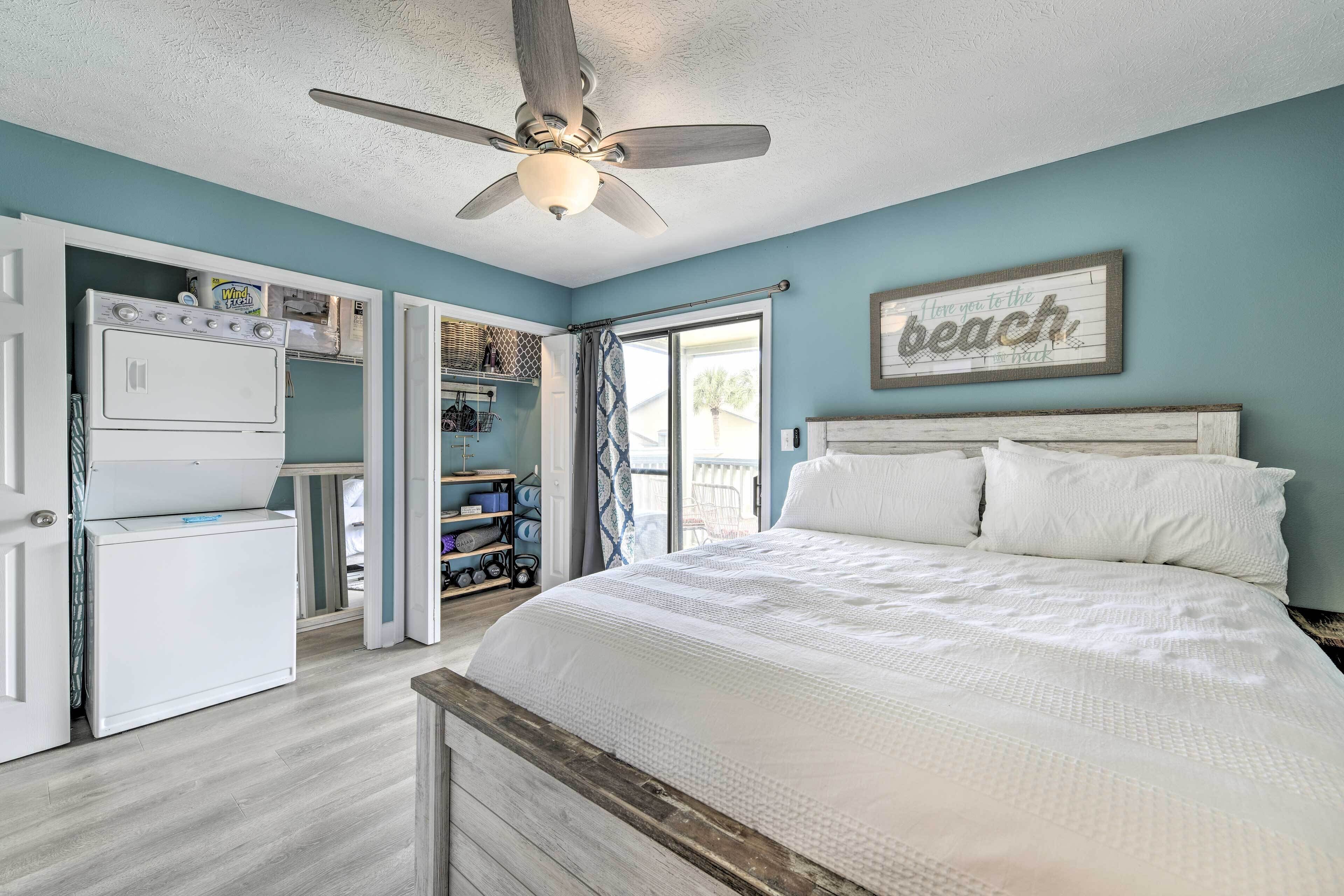 A bedroom with a bed, a ceiling fan, a refrigerator, and a window with a view of the outdoors.