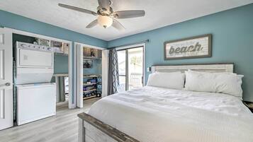 A bedroom with a bed, a ceiling fan, a refrigerator, and a window with a view of the outdoors.