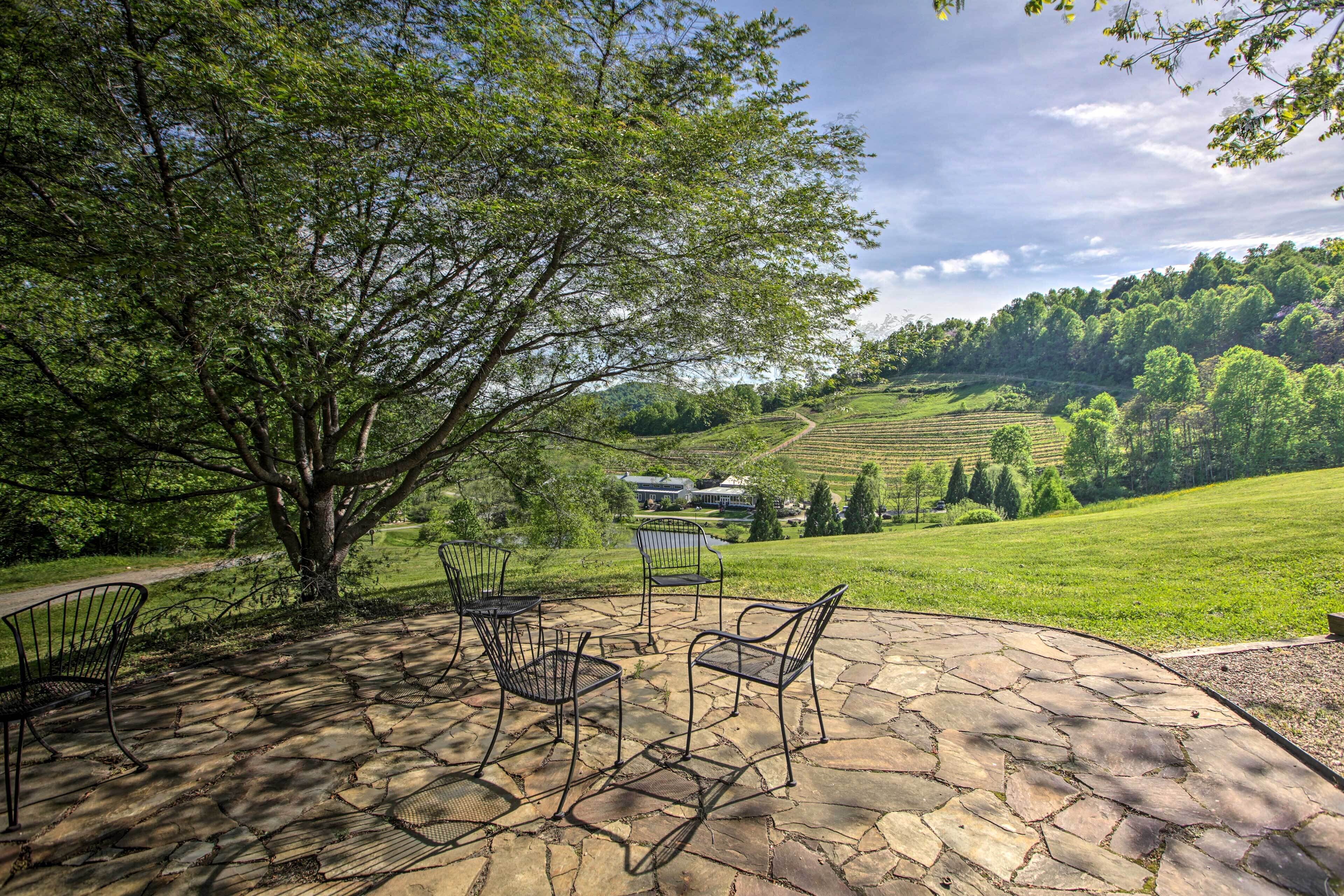 A stone patio with metal chairs and a large tree providing shade.
