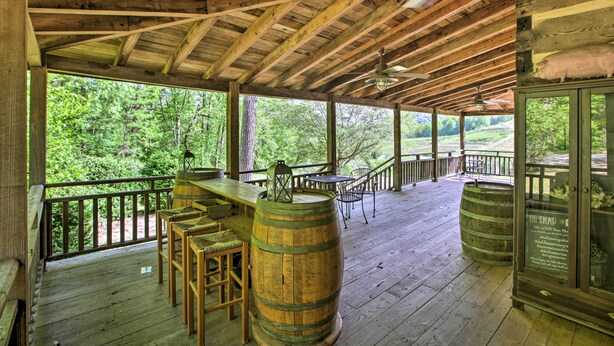 Una terraza de madera con zona de bar, asientos exteriores y un cerramiento de cristal que incluye un cerdo.