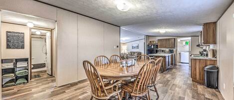 A spacious dining area with a wooden table and chairs, a kitchen in the background, and a hallway leading to a bathroom.