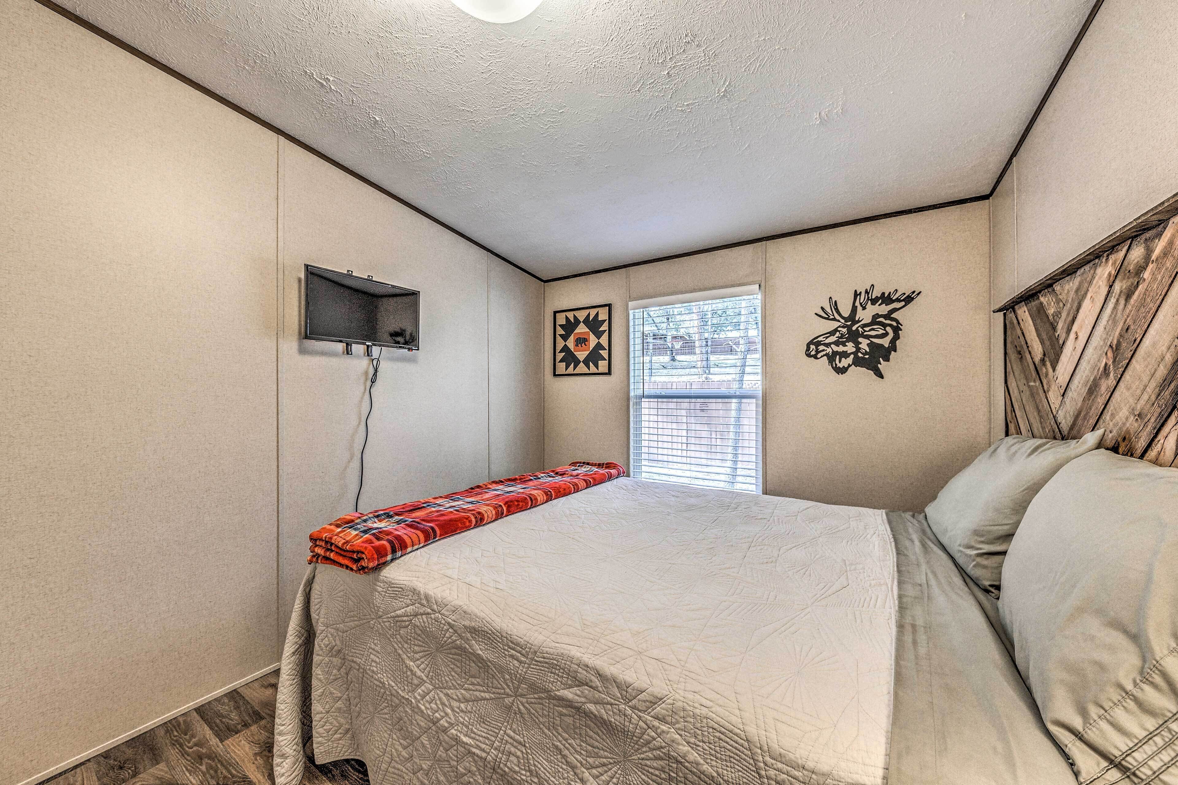 A bedroom with a bed, a small window, a wall-mounted TV, and a decorative wall piece.
