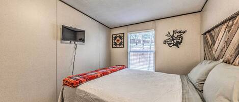 A bedroom with a bed, a small window, a wall-mounted TV, and a decorative wall piece.