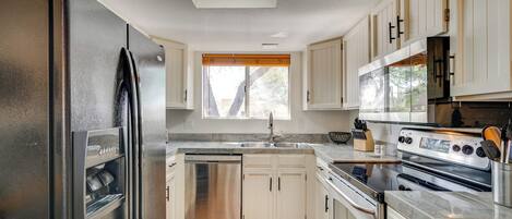 Una cocina moderna con electrodomésticos de acero inoxidable, armarios blancos y un amplio ventanal que proporciona luz natural.