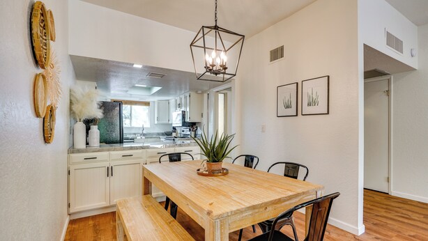 Un coin repas avec une table et des bancs en bois, des meubles blancs et un luminaire suspendu.