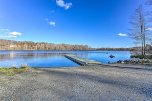 A gravel beach leading to a calm lake with a wooden dock extending into the water.