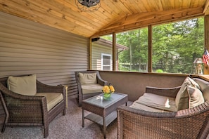 A covered porch with wicker furniture, a glass table, and a view of a house and trees.