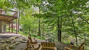 A forested outdoor area with Adirondack chairs and a small table, suggesting a natural setting for relaxation. - Riverview Big Bass Lake Poconos Retreat (Gouldsboro)